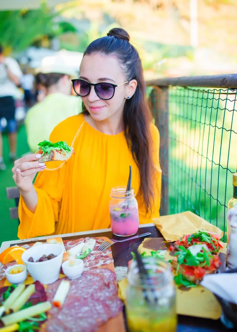 A woman in a yellow dress enjoying a delicious meal outdoors with a drink.